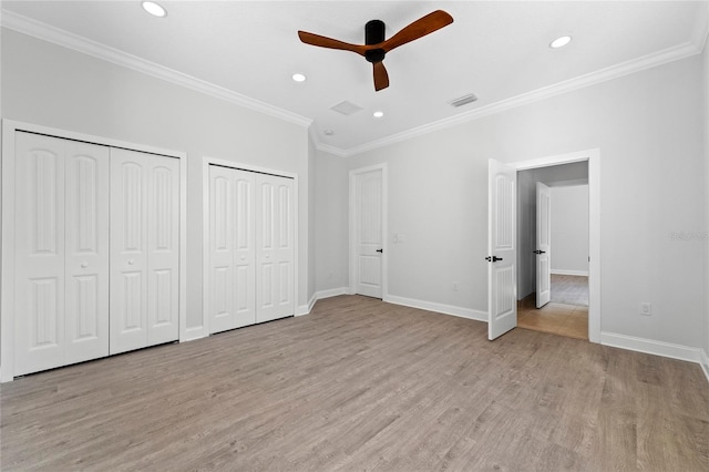 unfurnished bedroom featuring light wood-type flooring, ceiling fan, crown molding, and two closets