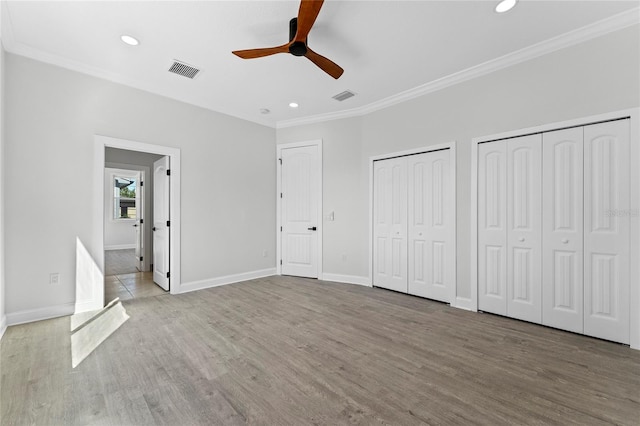 unfurnished bedroom featuring two closets, ceiling fan, crown molding, and wood-type flooring