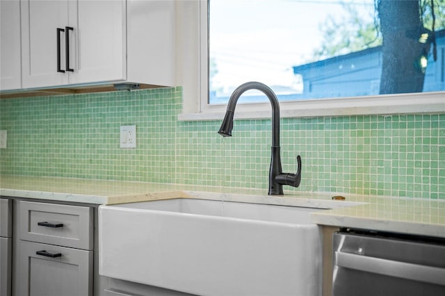 kitchen with white cabinetry, sink, light stone countertops, stainless steel dishwasher, and decorative backsplash