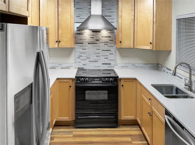 kitchen featuring appliances with stainless steel finishes, sink, wall chimney range hood, and light hardwood / wood-style floors