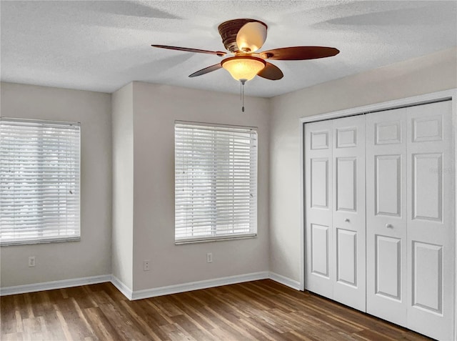 unfurnished bedroom with multiple windows, dark hardwood / wood-style floors, a closet, and ceiling fan