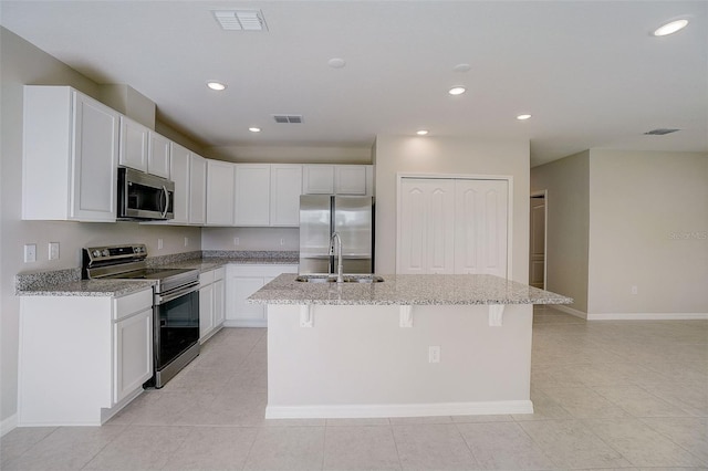 kitchen featuring a center island with sink, appliances with stainless steel finishes, light stone countertops, and white cabinetry