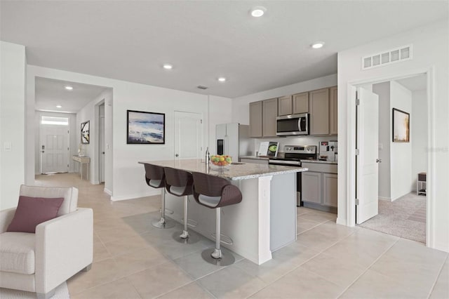 kitchen with a breakfast bar area, a kitchen island with sink, light stone countertops, light tile patterned flooring, and stainless steel appliances