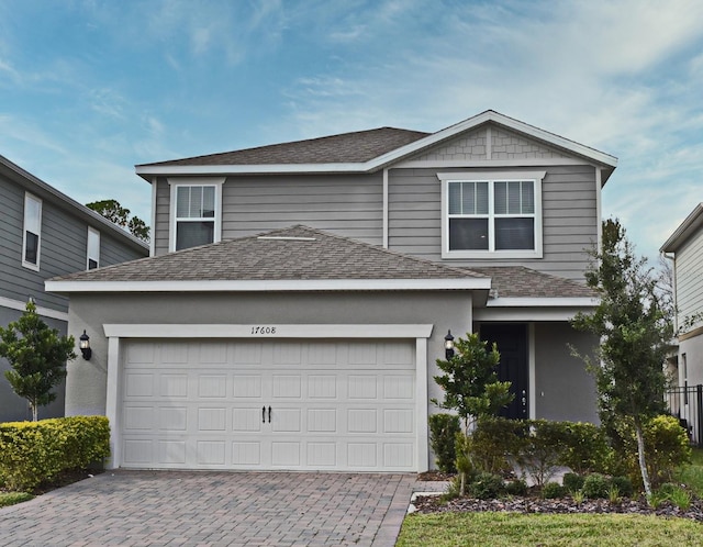 traditional-style house featuring an attached garage, a shingled roof, and decorative driveway