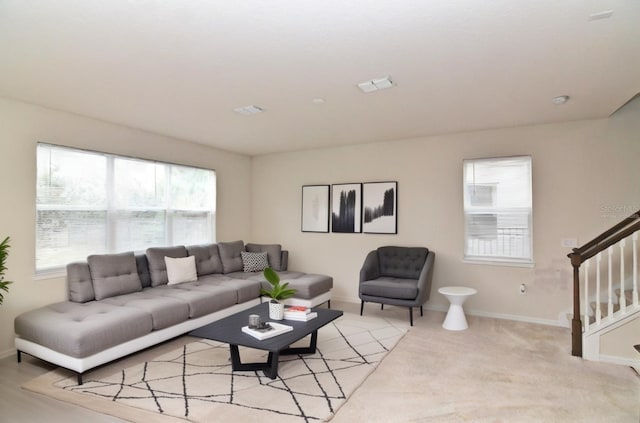 living area with stairway, baseboards, visible vents, and light carpet