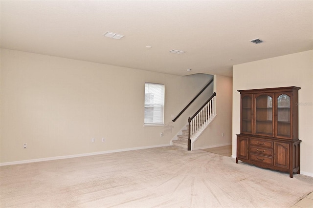 empty room with stairway, baseboards, light colored carpet, and visible vents