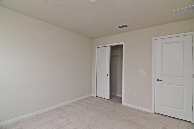 unfurnished bedroom featuring light carpet, a closet, and a textured ceiling