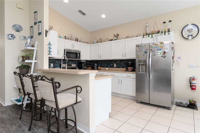 kitchen featuring kitchen peninsula, vaulted ceiling, a kitchen bar, white cabinetry, and appliances with stainless steel finishes