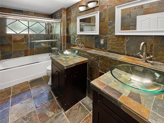 full bathroom with vanity, toilet, tile walls, and shower / bath combination with glass door