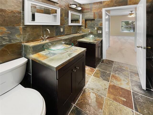 1711 Shadow View Cir Unit 1711, Maitland, FL 32751 - bathroom featuring a ceiling fan, stone finish flooring, tile walls, two vanities, and toilet