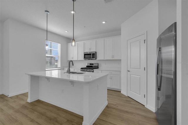 kitchen with sink, an island with sink, pendant lighting, stainless steel appliances, and white cabinets