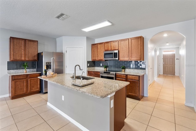 kitchen with backsplash, a textured ceiling, a kitchen island with sink, sink, and stainless steel appliances