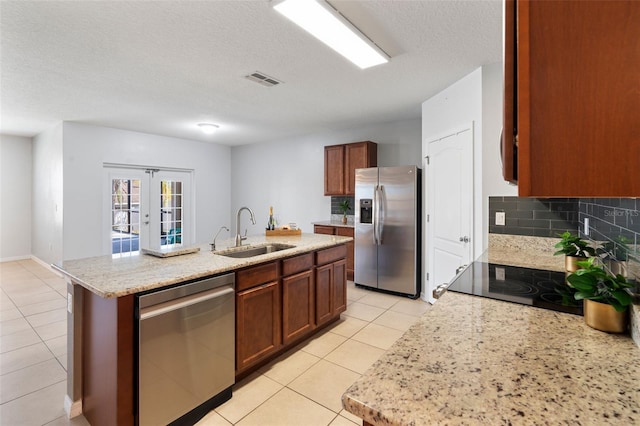 kitchen with appliances with stainless steel finishes, sink, a kitchen island with sink, a textured ceiling, and french doors