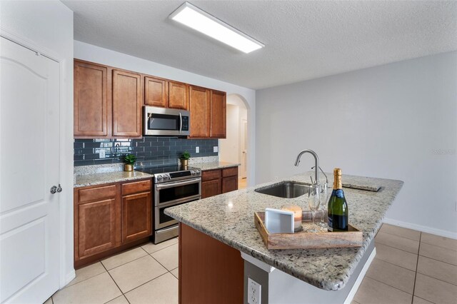 kitchen with sink, light tile patterned flooring, an island with sink, and appliances with stainless steel finishes