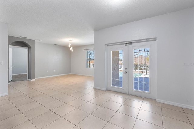 empty room featuring french doors, a textured ceiling, and light tile patterned floors
