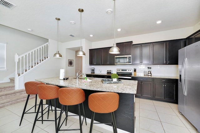 kitchen with a kitchen breakfast bar, a center island with sink, sink, decorative light fixtures, and appliances with stainless steel finishes