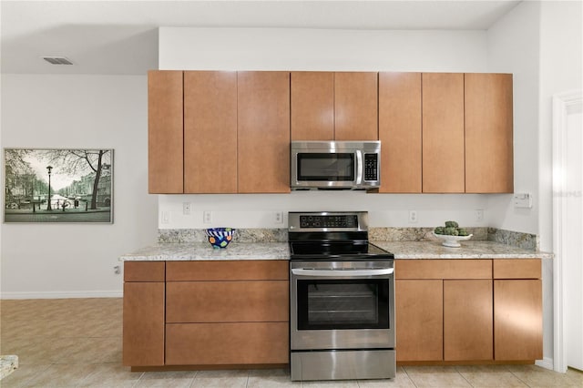 kitchen featuring brown cabinetry, light tile patterned floors, baseboards, and stainless steel appliances