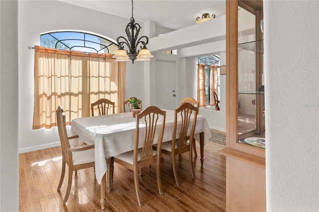 dining space with a wealth of natural light, an inviting chandelier, baseboards, and wood finished floors