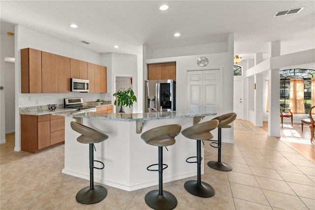 kitchen with a breakfast bar area, stainless steel appliances, visible vents, light tile patterned flooring, and an island with sink