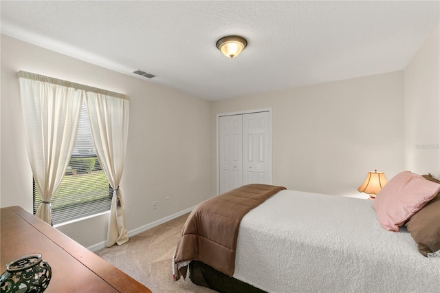 bedroom featuring light carpet, baseboards, visible vents, a textured ceiling, and a closet