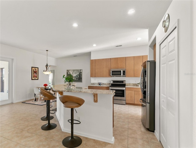 kitchen featuring light tile patterned floors, a kitchen breakfast bar, light stone countertops, stainless steel appliances, and pendant lighting