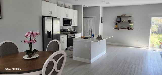 kitchen with sink, light hardwood / wood-style floors, stainless steel appliances, white cabinets, and a center island with sink