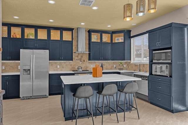 kitchen featuring stainless steel appliances, blue cabinetry, a center island, pendant lighting, and wall chimney exhaust hood