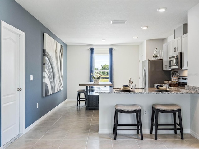 kitchen with kitchen peninsula, a kitchen breakfast bar, white cabinetry, stone countertops, and stainless steel appliances