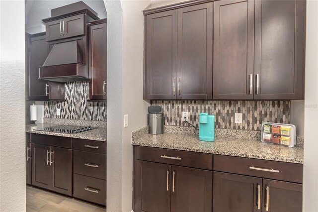 kitchen with black electric cooktop, light stone countertops, dark brown cabinetry, custom exhaust hood, and tasteful backsplash