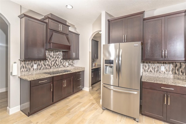 kitchen with decorative backsplash, premium range hood, stainless steel refrigerator with ice dispenser, and light wood-type flooring