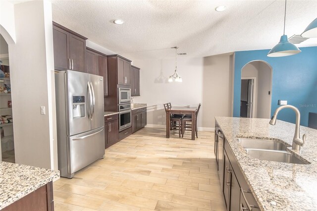 kitchen featuring hanging light fixtures, stainless steel appliances, sink, and light wood-type flooring