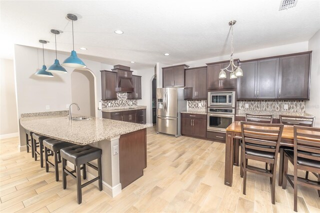 kitchen with appliances with stainless steel finishes, sink, light hardwood / wood-style floors, pendant lighting, and decorative backsplash