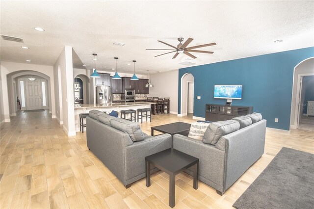 living room featuring a textured ceiling, light wood-type flooring, and ceiling fan