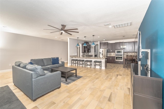 living room featuring a textured ceiling, light wood-type flooring, and ceiling fan