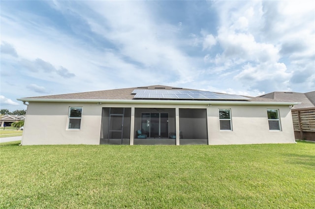 rear view of house with a sunroom, a lawn, and solar panels