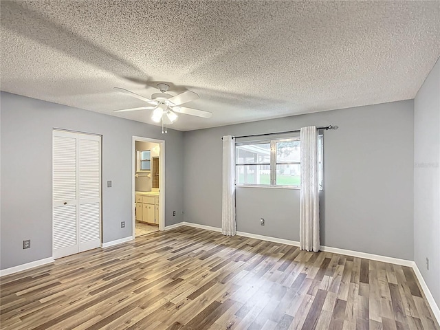 unfurnished bedroom with ceiling fan, a textured ceiling, light wood-type flooring, a closet, and ensuite bath