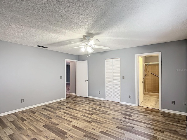 unfurnished bedroom featuring ceiling fan, ensuite bathroom, a textured ceiling, and hardwood / wood-style floors