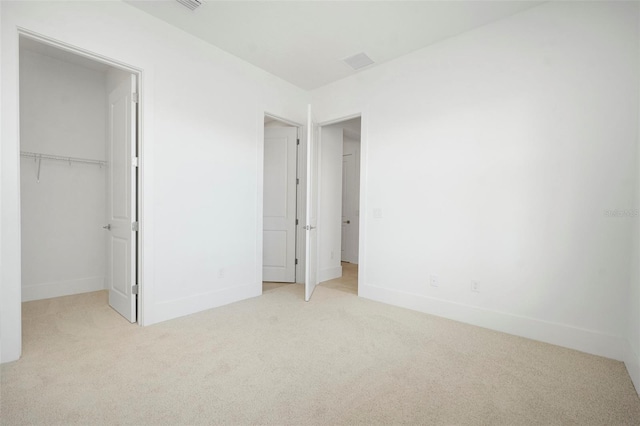 unfurnished bedroom with a walk in closet, light colored carpet, and a closet