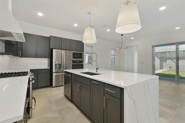 kitchen with premium range hood, sink, hanging light fixtures, stainless steel appliances, and a kitchen island with sink