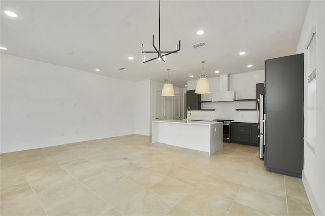 kitchen featuring appliances with stainless steel finishes, pendant lighting, tasteful backsplash, a center island with sink, and wall chimney range hood