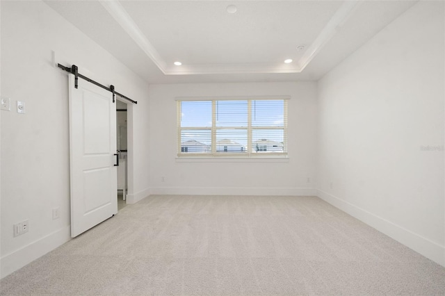 unfurnished bedroom with a barn door, light colored carpet, and a tray ceiling