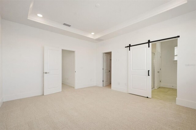 unfurnished bedroom with a tray ceiling, light colored carpet, a barn door, and a spacious closet