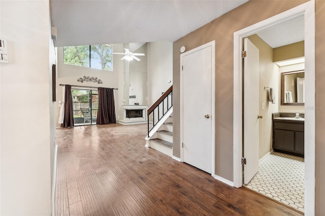 foyer entrance with ceiling fan, a textured ceiling, wood-type flooring, a towering ceiling, and sink