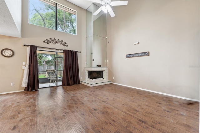 unfurnished living room with a tiled fireplace, hardwood / wood-style flooring, a healthy amount of sunlight, and a high ceiling