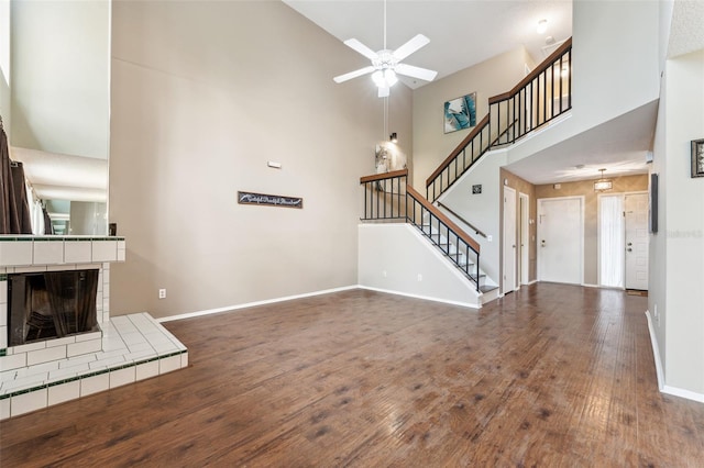 unfurnished living room featuring a fireplace, dark hardwood / wood-style floors, a towering ceiling, and ceiling fan