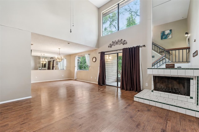 unfurnished living room with a towering ceiling, a textured ceiling, hardwood / wood-style floors, a tiled fireplace, and a chandelier