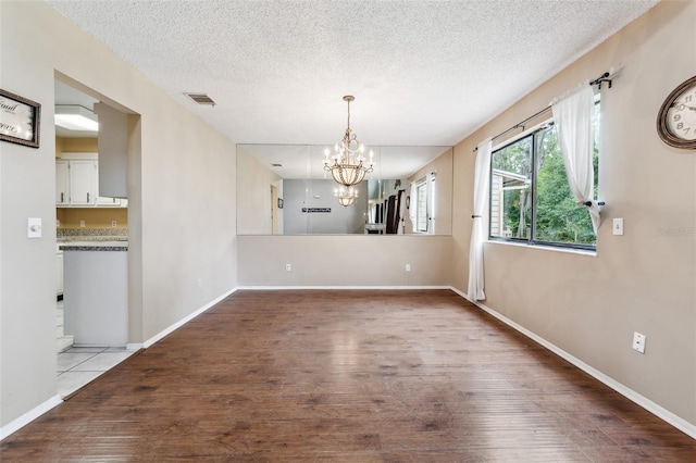 unfurnished dining area with light hardwood / wood-style floors, a textured ceiling, and a chandelier