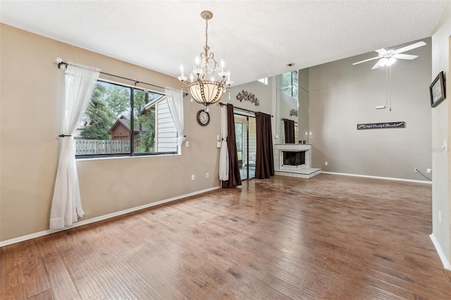 unfurnished living room with a textured ceiling, ceiling fan with notable chandelier, hardwood / wood-style flooring, and a tile fireplace