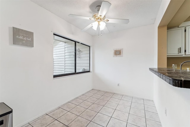 unfurnished dining area with ceiling fan, a textured ceiling, and light tile patterned floors