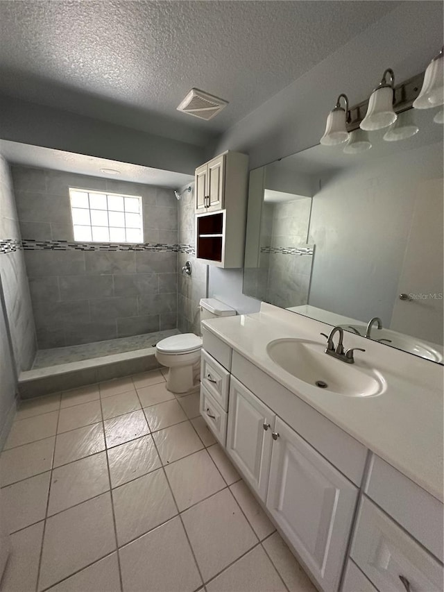 bathroom with a tile shower, a textured ceiling, toilet, vanity, and tile patterned floors